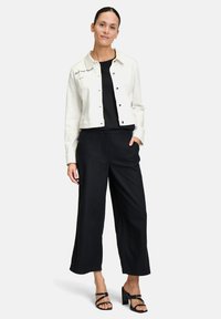 Veste en denim blanche avec des boutons noirs, t-shirt noir et pantalon large noir ample. Des sandales à talons avec des brides noires complètent le look.