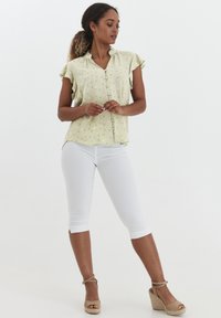 Hellgrüne Bluse mit kurzen Ärmeln, Blumenmuster, Knopfverschluss und gerafftem Ausschnitt. Kombiniert mit weißen Caprihosen und beigen Wedgesandaletten.