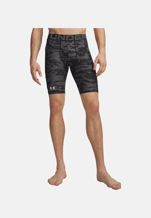 Mand iført sorte og grå camouflage kompressionstrusser med stor tekst på taljebåndet og hvidt Under Armour-logo på venstre lår.