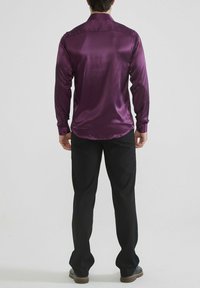 Chemise longue en satin violet à manches longues avec poignets à boutons, présentant une texture lisse et un col classique, assortie à un pantalon et des chaussures noirs.