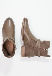 Botas de tobillo marrones hechas de cuero y ante, que presentan un cierre de cremallera lateral, un acabado texturizado, un tacón bajo apilado y un detalle de correa en contraste.