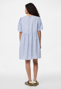 Ανοιχτό μπλε φόρεμα με ριγέ μοτίβο, κοντά φουσκωτά μανίκια, μαζεμένη μέση και μικρές κόκκινες λουλουδίσιες λεπτομέρειες. Φορεμένο με casual αθλητικά παπούτσια.