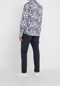 Camicia a maniche lunghe con base bianca e motivo floreale blu; abbinata a pantaloni navy e sneakers bianche.