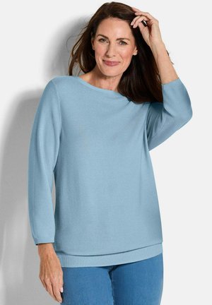 Hellblauer gestrickter Pullover mit einem Bootsausschnitt und Dreiviertelärmeln. Hat gerippte Bündchen und Saum, kombiniert mit blauen Jeans.
