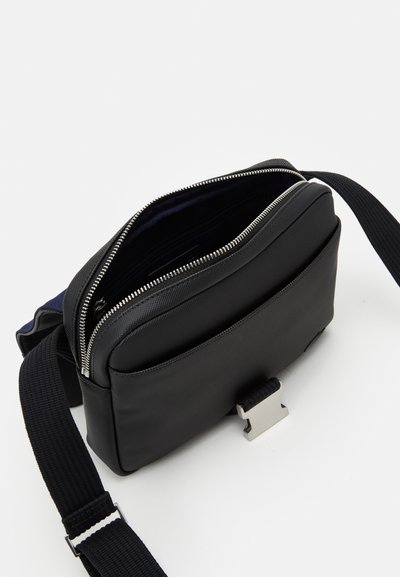Sac à épaule en tissu noir avec fermeture éclair, extérieur texturé, bandoulière réglable et accent en métal argenté. Vue de dessus ouverte.