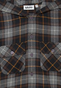 Rutigt flanellskjorta i grått, svart och brunt med orange detaljer. Har en huva, två bröstfickor och lila knappar.