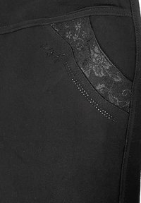 Schwarze Hosen aus strukturiertem Stoff, mit einem transparenten gemusterten Taillensack und silbernen Nieten entlang der Naht für akzentuierende Details.