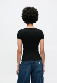 Czarny krótki rękaw koszulki o dopasowanym kroju, pokazany od tyłu, zestawiony z luźnymi niebieskimi dżinsami z dwoma tylnymi kieszeniami.