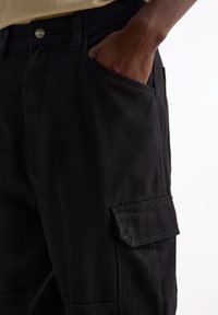 Pantaloni cargo neri realizzati in tessuto resistente, con tasca laterale, passanti per cintura e una vestibilità classica. Tessuto liscio con cuciture dettagliate.