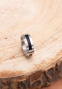 Metalen ring met een zilveren afwerking, voorzien van een centrale zwarte draad en een gegolfde rand, rustend op een houten oppervlak.