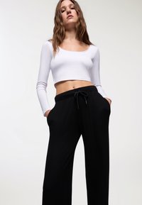 Top corto bianco a maniche lunghe abbinato a pantaloni a gamba larga neri a coste con vita elasticizzata e tasche laterali.