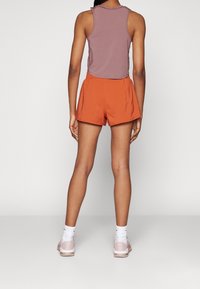 Top sin mangas de color púrpura y pantalones cortos naranjas, tela suave, corte relajado, longitud por encima de la rodilla, combinado con zapatillas rosas claras y calcetines blancos.