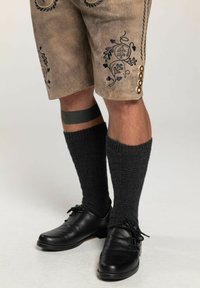 Braun gestickte Shorts mit dekorativer Naht, kombiniert mit dunkelgrauen knielangen Socken und schwarzen Schnürschuhen.