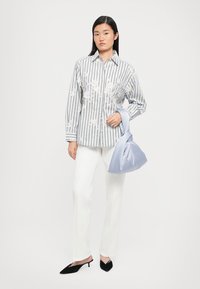 Cămășă rayată în alb și gri cu broderie florală, asortată cu pantaloni albi și o geantă moale de un albastru deschis. Pantofii negri cu vârf ascuțit completează ținuta.