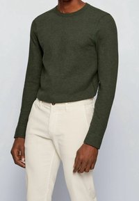 Grön långärmad tröja med ribbat mönster och rundad hals, kombinerad med ljusbeiga byxor; har en rak passform och enkel design.