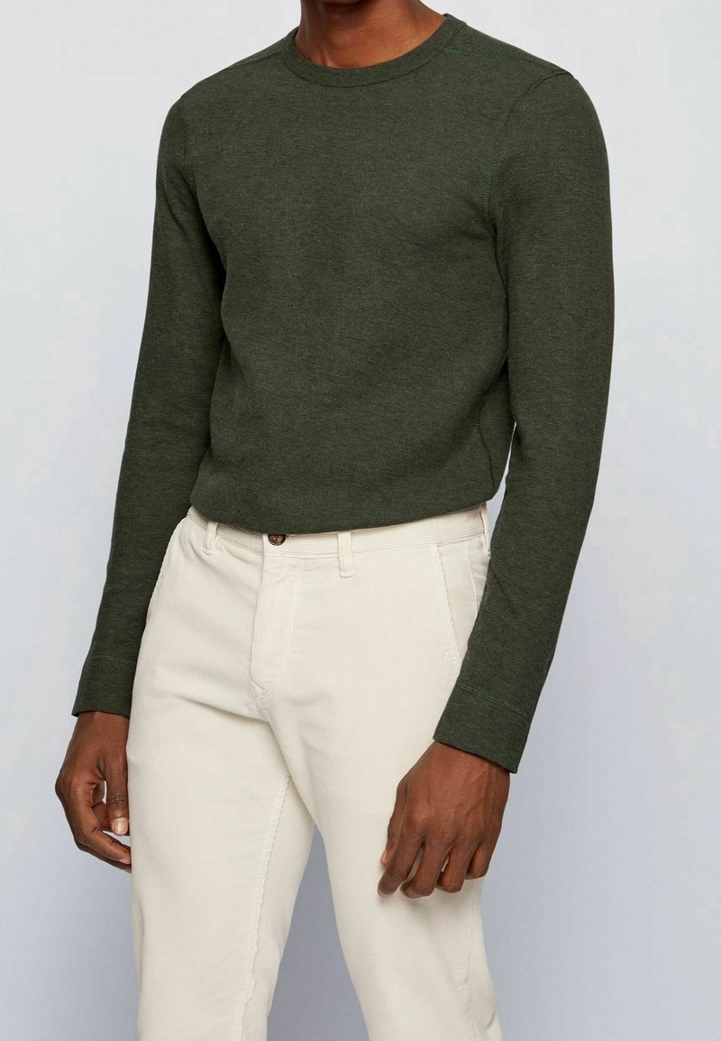 Grön långärmad tröja med ribbat mönster och rundad hals, kombinerad med ljusbeiga byxor; har en rak passform och enkel design.