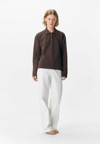Braunes langärmliges Polohemd mit drei Knöpfen, kombiniert mit weißen, weiten Hosen. Glatte Textur, lässiges Design.