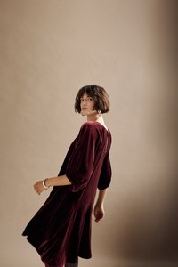 Bordeauxrotes Samtkleid mit lockerer Passform, Ballonärmeln und einem Schlüsselloch-Detail hinten. Glatte Textur, knielanger Saum.