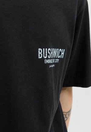 Black t-shirt with white cracked-text print saying "BUSHWICH Embrace the City" worn by a person with a visible tattoo on the arm.