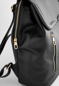 Sac à dos en cuir noir avec des zips dorés, des bretelles réglables et une poche zippée à l'avant sur un fond clair.