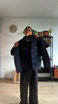 Tumma farkkutakki, jossa on kaksi rintataskua, hopeiset napit ja klassinen kaulus, henkilön yllä rento asu.