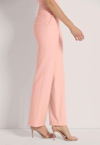 Lichtroze, high-waisted broek met een wijd model; lichtgewicht stof; gecombineerd met naakte, strapschoenen met hoge hakken.