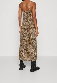 Maxiklänning med leopardmönster och tunna band, tillverkad av ett lättviktigt tyg. Svarta ankelstövlar synliga i botten.