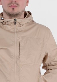 Giubbotto leggero beige con cappuccio, dotato di una cerniera frontale completa e di una grande tasca quadrata sul petto. Tessuto dalla texture liscia e opaca.