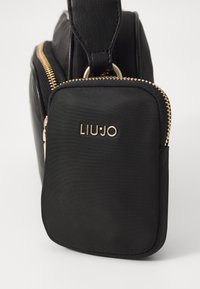 Schwarze Handtasche mit strukturiertem Oberflächen, ausgestattet mit einem auffälligen Reißverschluss in Goldtönen und Markierungslogo. Kompakte Bauweise mit runder Form und Griff.