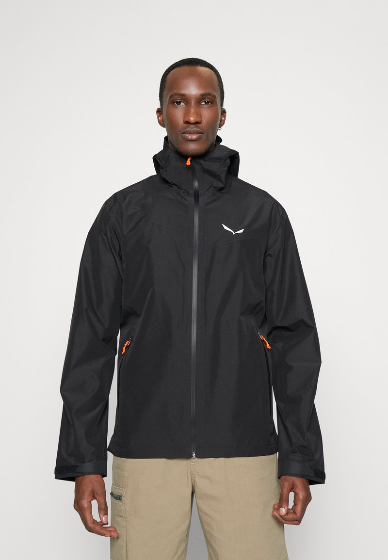 Veste imperméable noire avec un col haut, fermeture éclair, accents orange et un logo sur la poitrine ; dispose de poches des deux côtés.