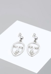 Orecchini in argento con un design minimalista a forma di volto, dettagli intagliati, una perlina rotonda come accent alla sommità e una finitura lucida.