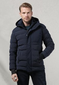 Giacca imbottita blu navy con cappuccio, dotata di chiusura con zip, due tasche laterali e polsini elastici per una vestibilità aderente. Tessuto liscio.
