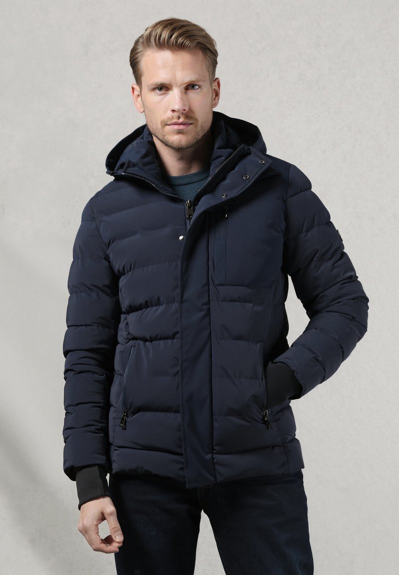 Giacca imbottita blu navy con cappuccio, dotata di chiusura con zip, due tasche laterali e polsini elastici per una vestibilità aderente. Tessuto liscio.