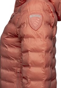 Perzikkleurige pufferjack met een quilted ontwerp. Heeft een getextureerde Blauer logo patch op de schouder en verborgen zijzakken.