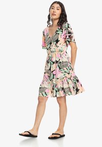Robe courte florale avec un décolleté en V, des manches volantées, une taille élastique et un ourlet volanté dans des nuances de rose, vert et noir.