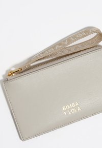 Cartera de muñeca de piel beige clara con cremallera dorada y logo "BIMBA Y LOLA" en letras doradas en la parte frontal.