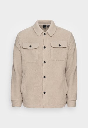 Giacca in pile beige con colletto, due tasche sul petto con bottoni neri e chiusura frontale con bottoni neri.