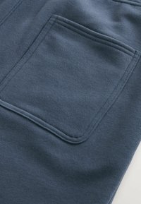 Pantalones de chándal azul marino con una textura suave, que cuentan con un bolsillo trasero y costuras planas. La tela parece duradera y ligeramente elástica.