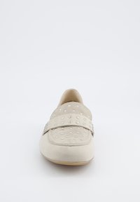 Mocassino in pelle scamosciata beige con una fascia ampia decorata da borchie metalliche in rilievo, punta rotonda e suola liscia. Design minimalista e texture morbida.