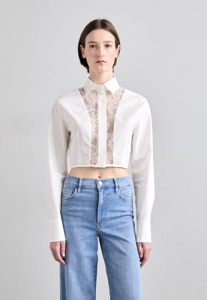Witte cropped shirt met kantpaneel aan de voorkant, lange mouwen en een kraag. Gecombineerd met lichtblauwe, wijde denim jeans.