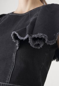 Svart denimkjole med volangermarmer med frynsete kanter og kontrastsøm. Nærbilde som fremhever tekstur og designdetaljer.