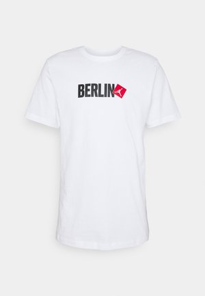 Biała koszulka z krótkim rękawem i okrągłym dekoltem z napisem „BERLIN” oraz czerwonym kwadratowym logo z postacią skaczącą na piersi.