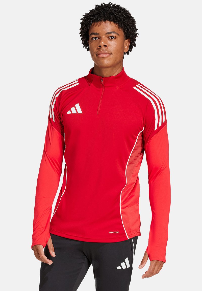 Maglia sportiva rossa a maniche lunghe con zip a mezze, accenti bianchi e tre strisce bianche sulle spalle. Realizzata in tessuto traspirante.