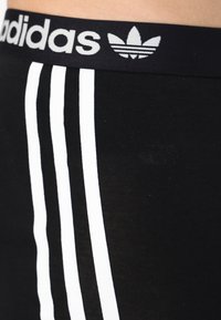 Sorte atletiske leggings med en bred svart midje med grå "adidas"-tekst og logo, supplert med tre hvite vertikale striper.