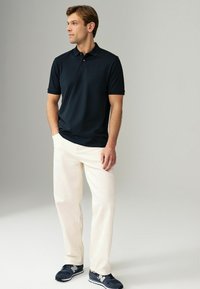Mørkeblå polo med krave, cremefarvede bukser og mørke sportssko. Overtøjet har et enkelt design og en afslappet pasform.