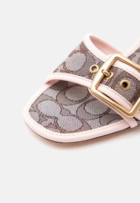 Πέδιλο ανοιχτής μύτης με μπεζ ύφασμα με σχέδια, ροζ λεπτομέριες και μια μεγάλη χρυσή αγκράφα στο λουράκι.