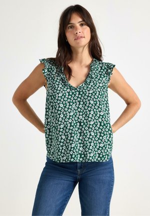 Grøn blomsterbluse med hvide blomster, v-udskæring og flæseærmer. Sammen med blå denim jeans.