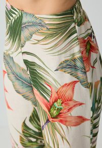 I pantaloni floreali presentano un tessuto leggero con grandi foglie verdi e fiori rossi vivaci. Il design include una comoda cintura elastica.