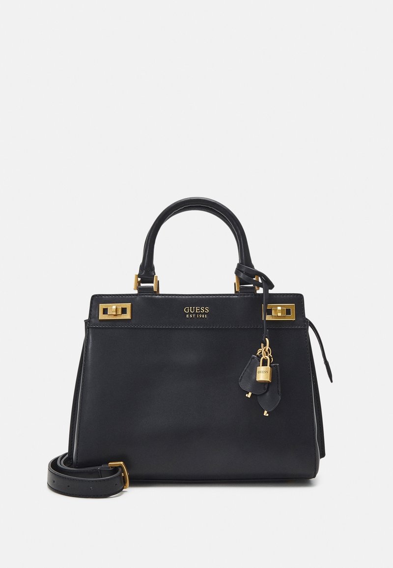 Sac à main Guess en cuir noir avec ferrures dorées, poignées supérieures, une bandoulière amovible et un petit détail de cadenas et clé suspendu.