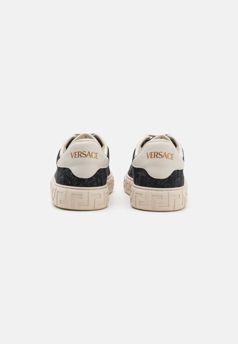 Sneaker neri e crema con branding Versace, tessuto testurizzato e suola in gomma decorata con un distintivo design a chiave greca.